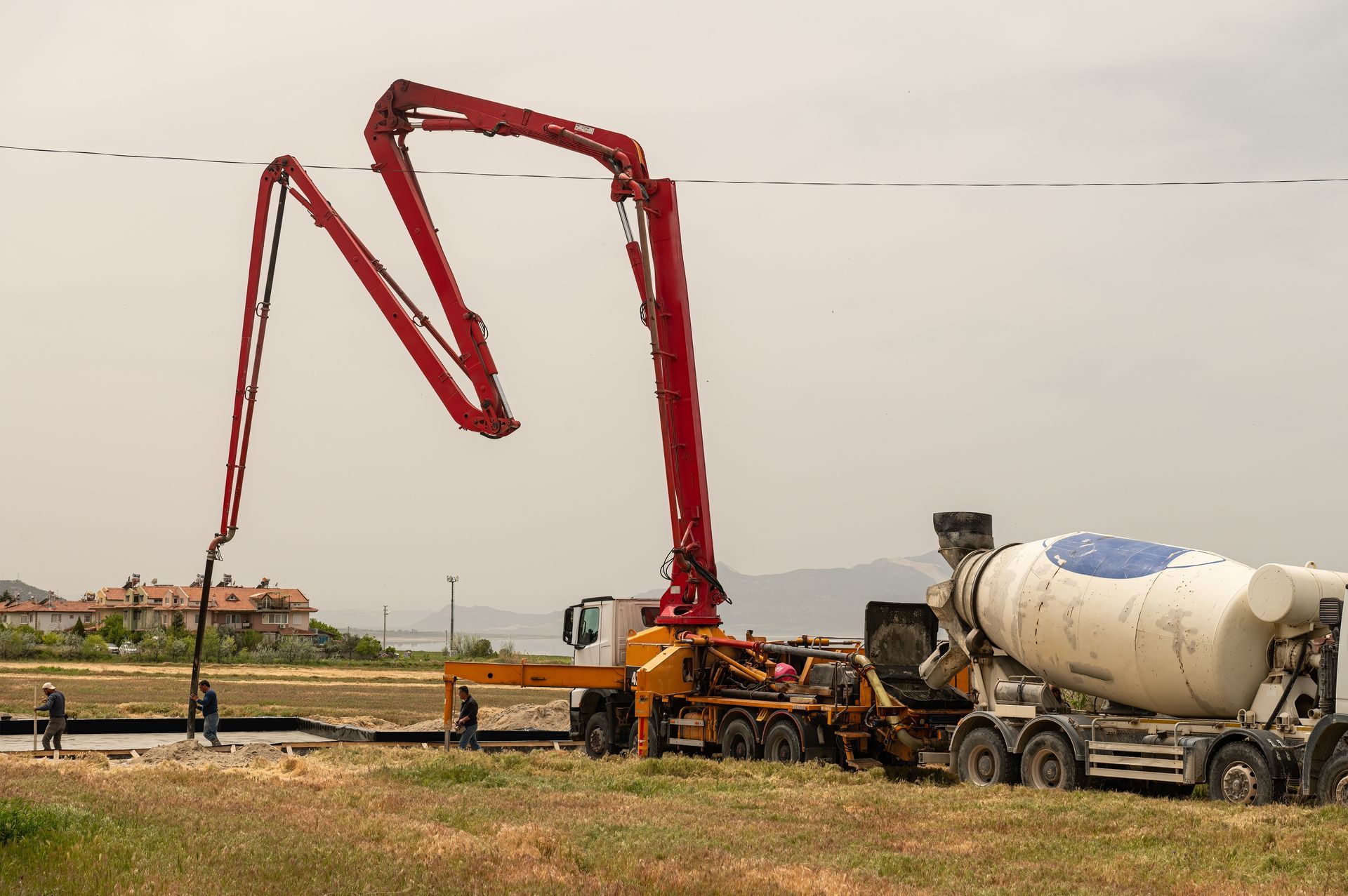A Red Concrete Pump Truck Extending Over a Construction Site — Far Northern Concrete Pumping in Tablelands, QLD