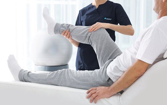 Terapista che aiuta un paziente a muovere le gambe. Il paziente è sdraiato su un lettino