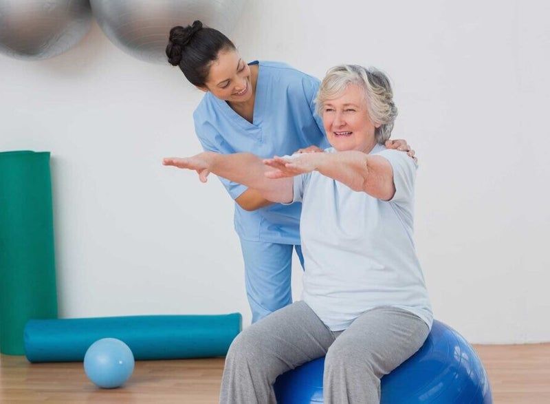 Donna che fa esercizio su una palla, guidata da un medico in palestra.