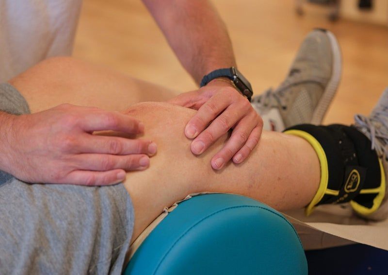 Il ginocchio di una persona viene esaminato dalle mani di un terapista