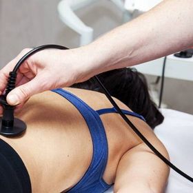 Persona sottoposta a terapia sdraiata sulla schiena, tenuta per mano; cavo nero ed elettrodo visibili.