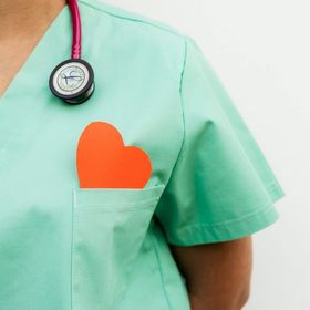 Infermiera che indossa un camice verde, uno stetoscopio e un cuore rosso in tasca.