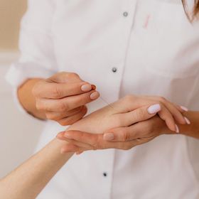 Mani che eseguono l'agopuntura sul polso di una persona. L'operatore indossa un camice bianco.