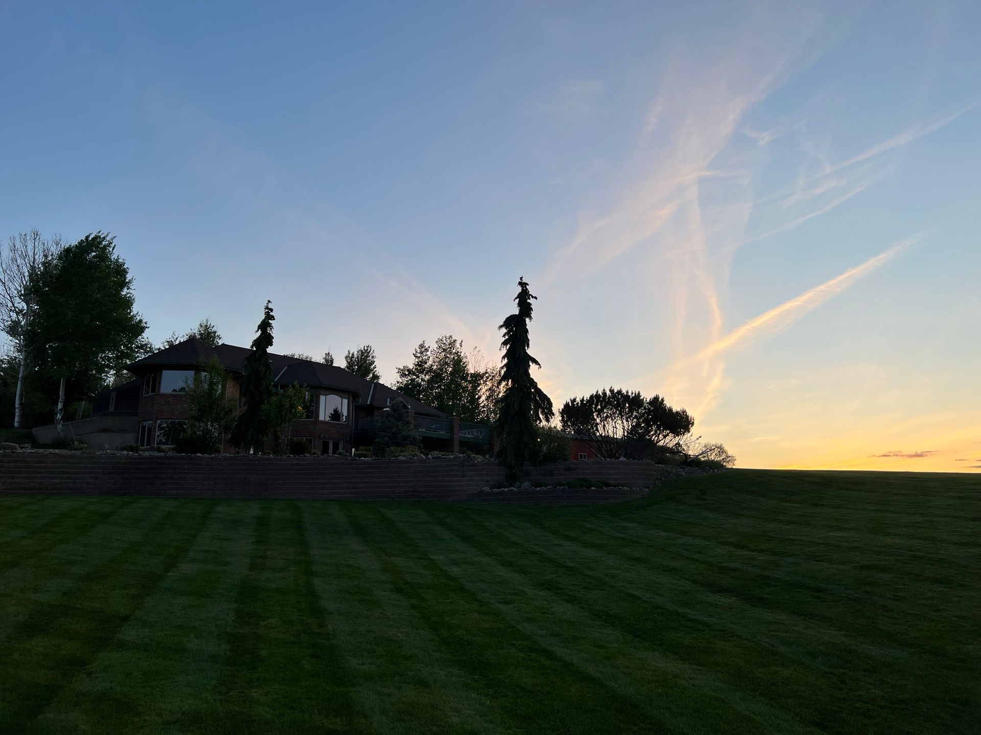 House on a hill with freshly mowed green lawn under a blue and orange sunset sky.