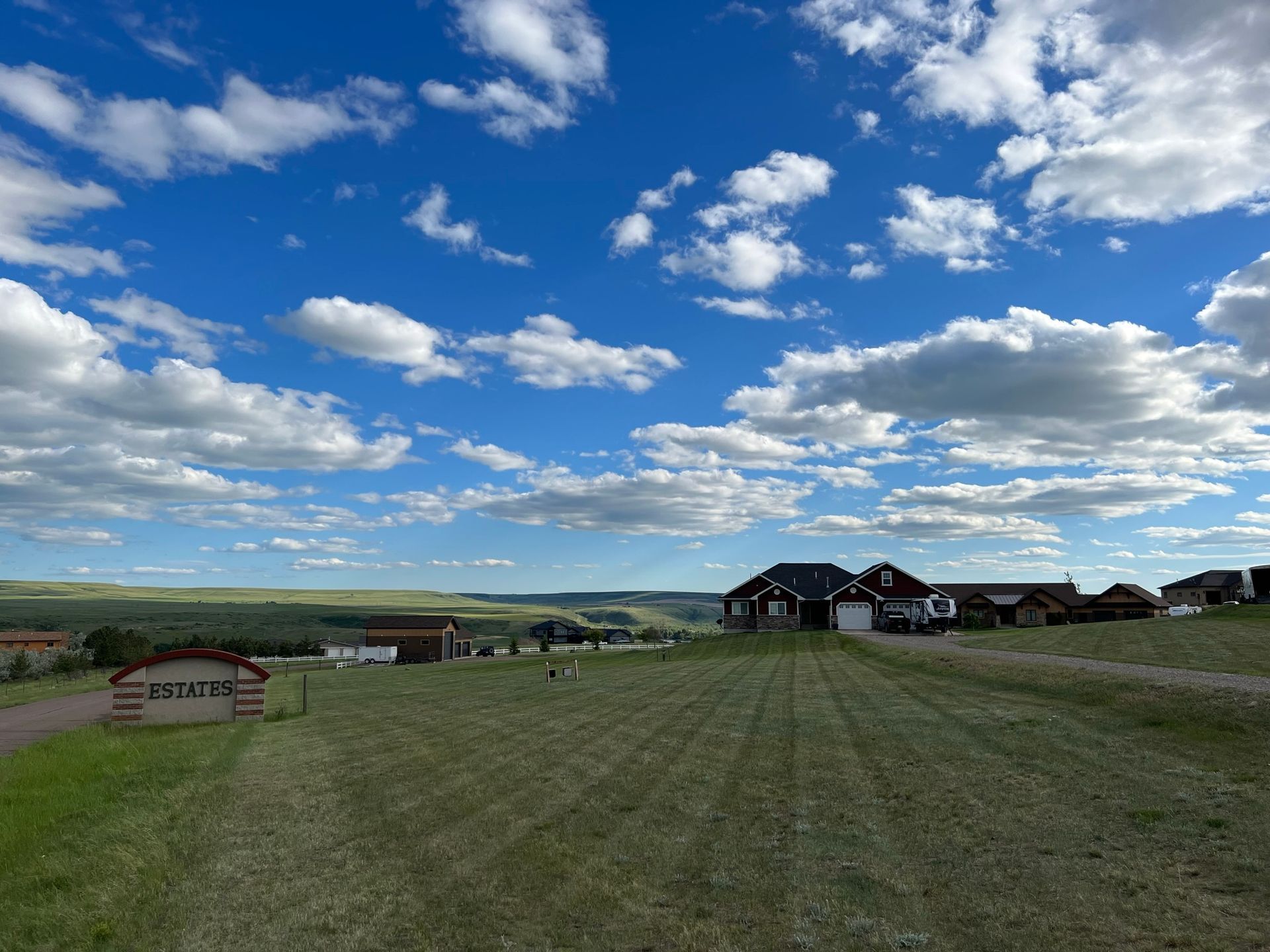 Blue sky with fluffy clouds over a green field, houses, and a sign that says 