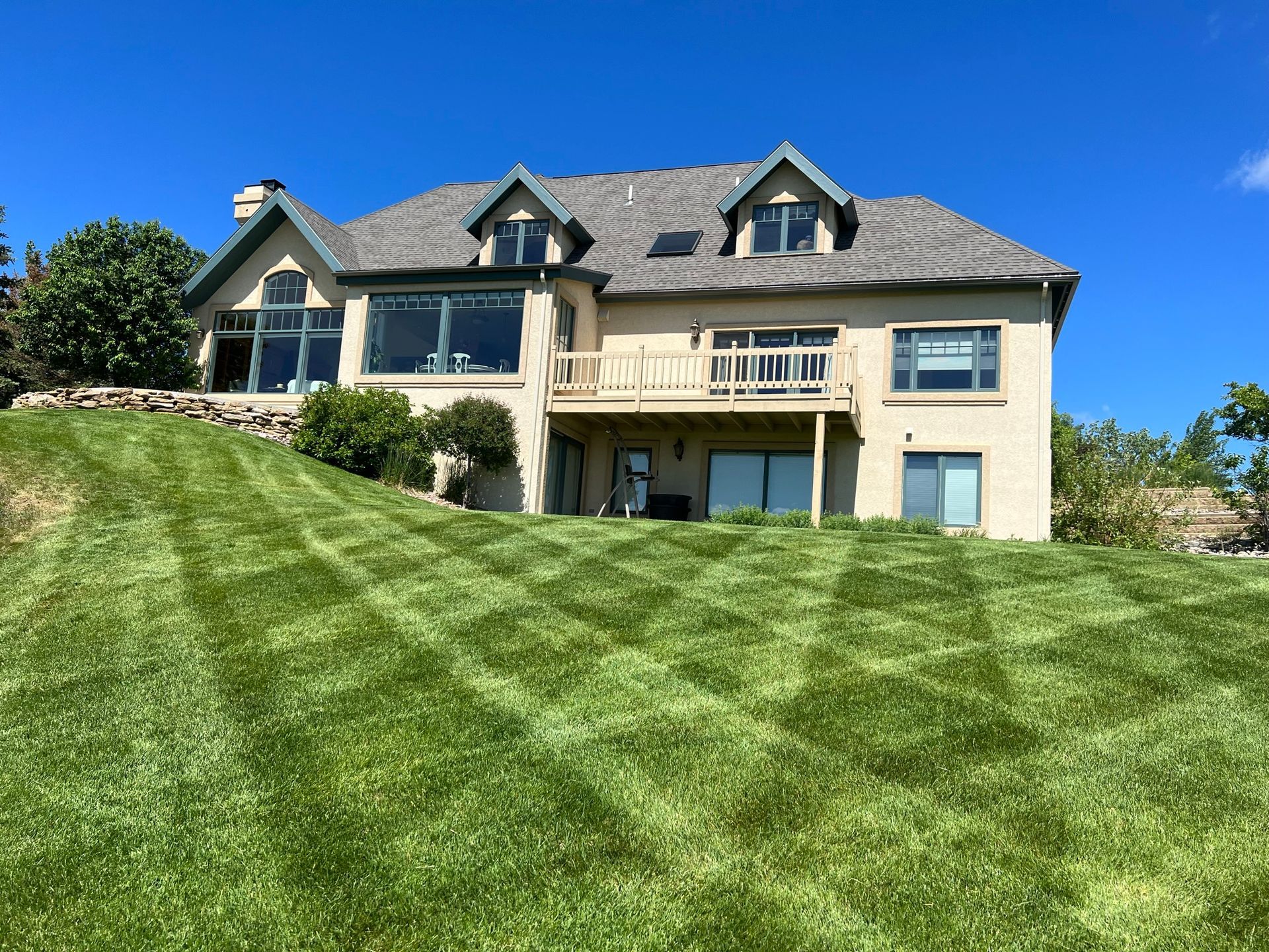 House with a green lawn cut in a pattern, blue sky.