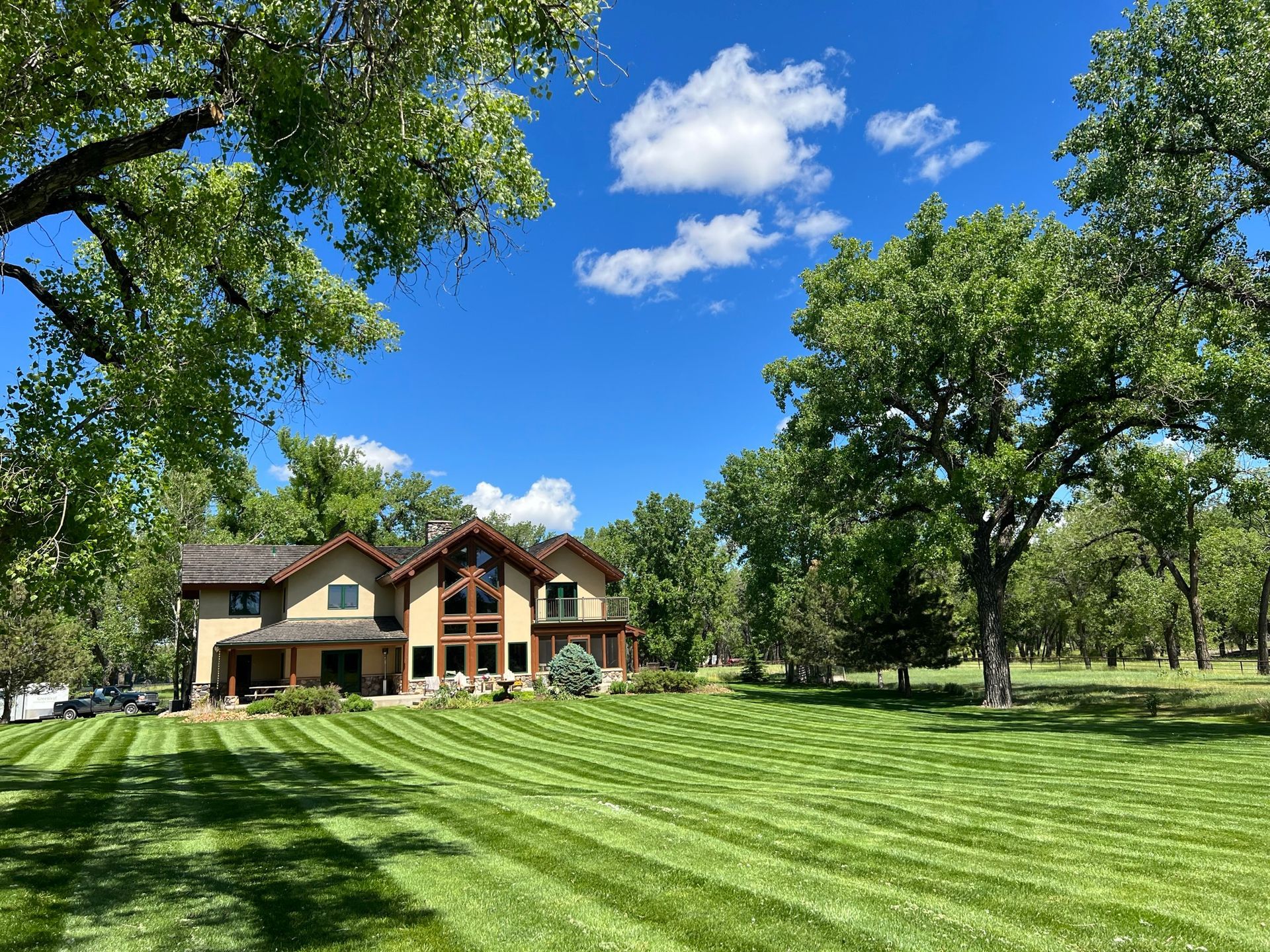 A large house with a well-manicured lawn under a blue sky, framed by trees.