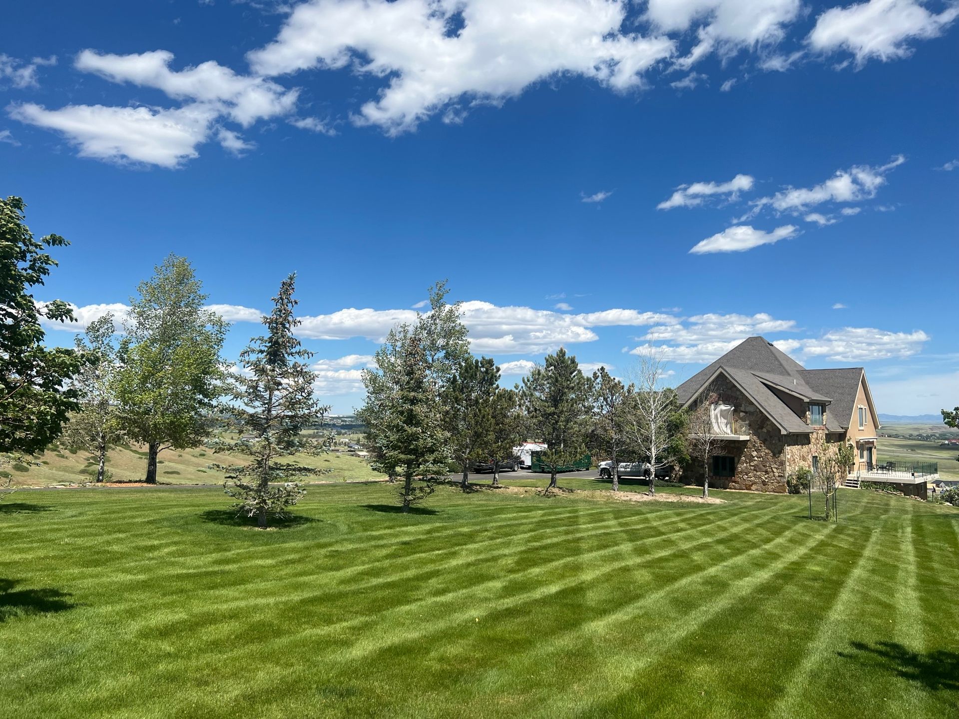 Lawn with stripes in front of a large house on a sunny day, under a blue sky with clouds.