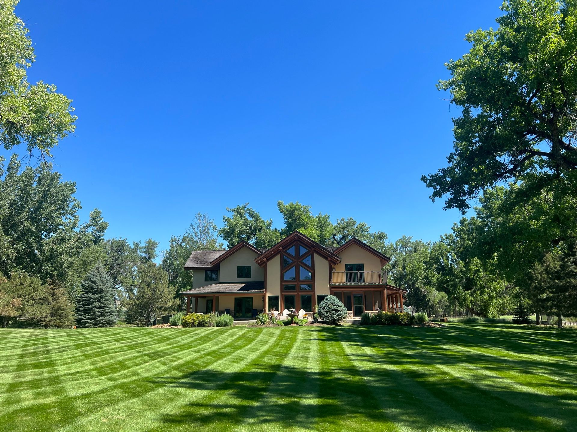 Large house with a manicured lawn, framed by trees, under a bright blue sky.