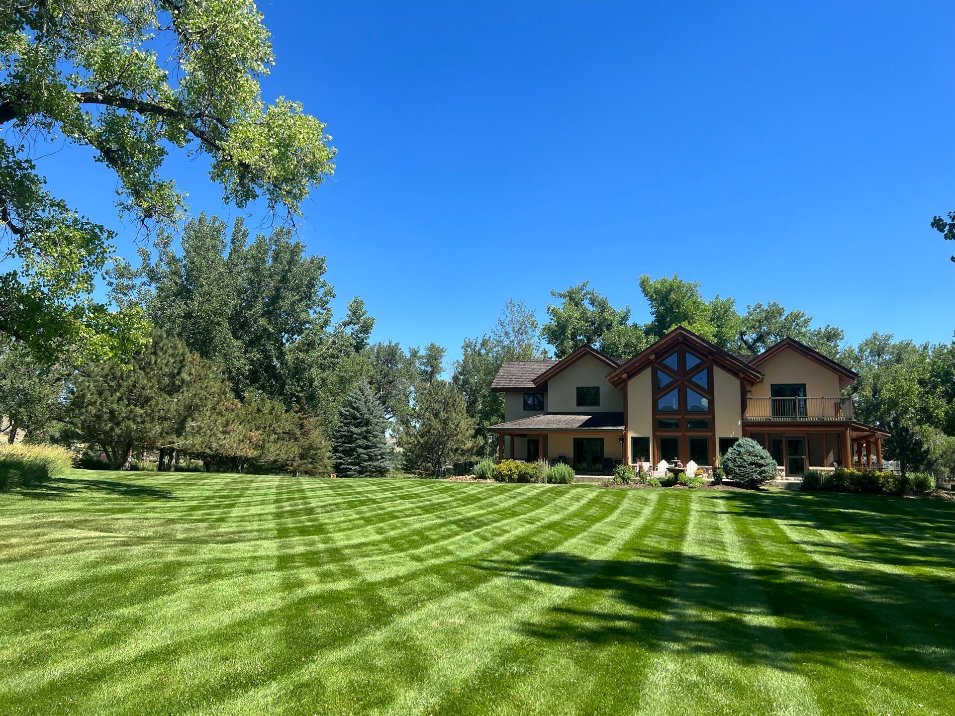 Large house with a well-manicured lawn under a blue sky; trees in the background.