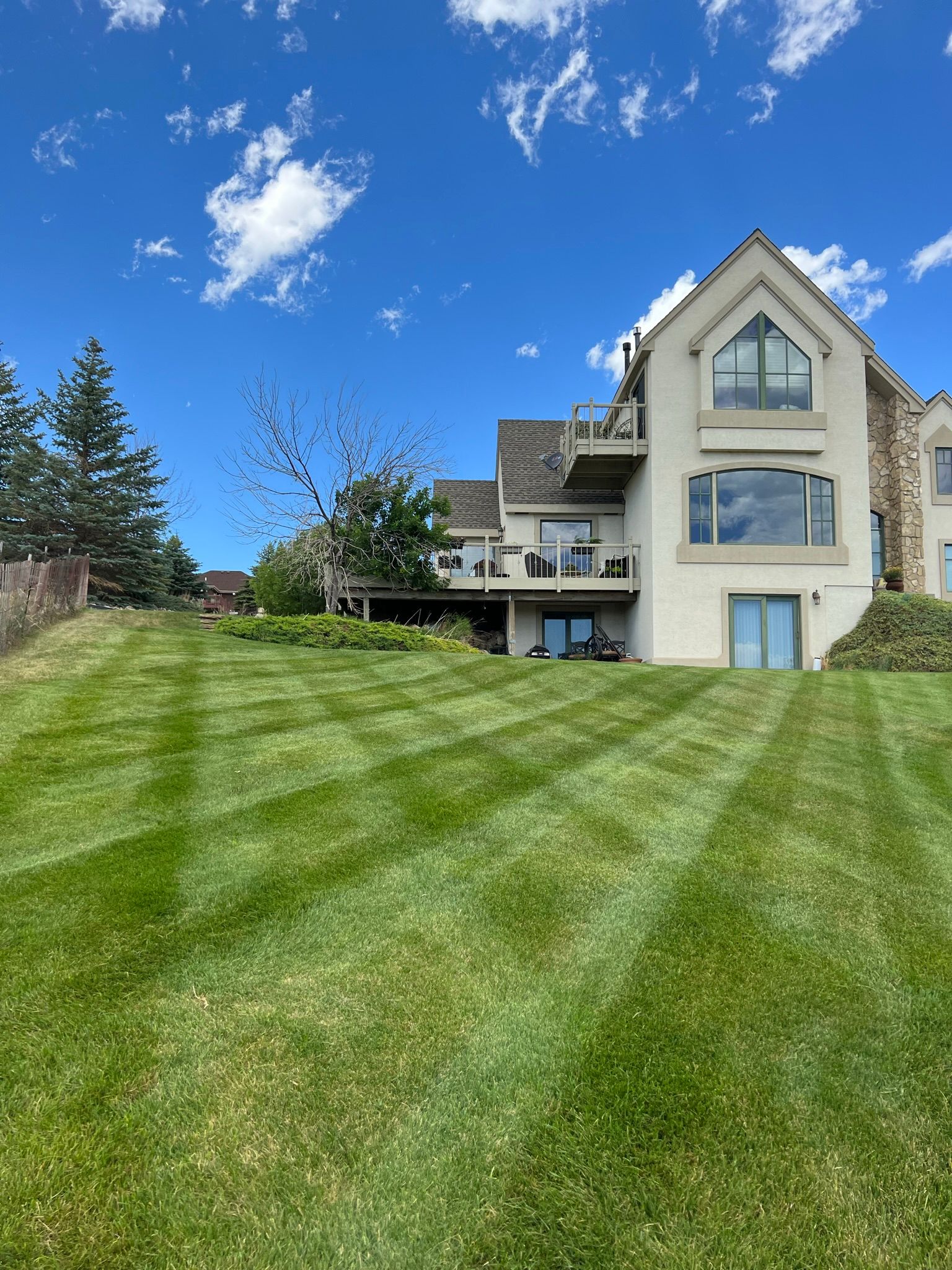 Lush green lawn with striped mowing pattern in front of a multi-story beige house on a sunny day.