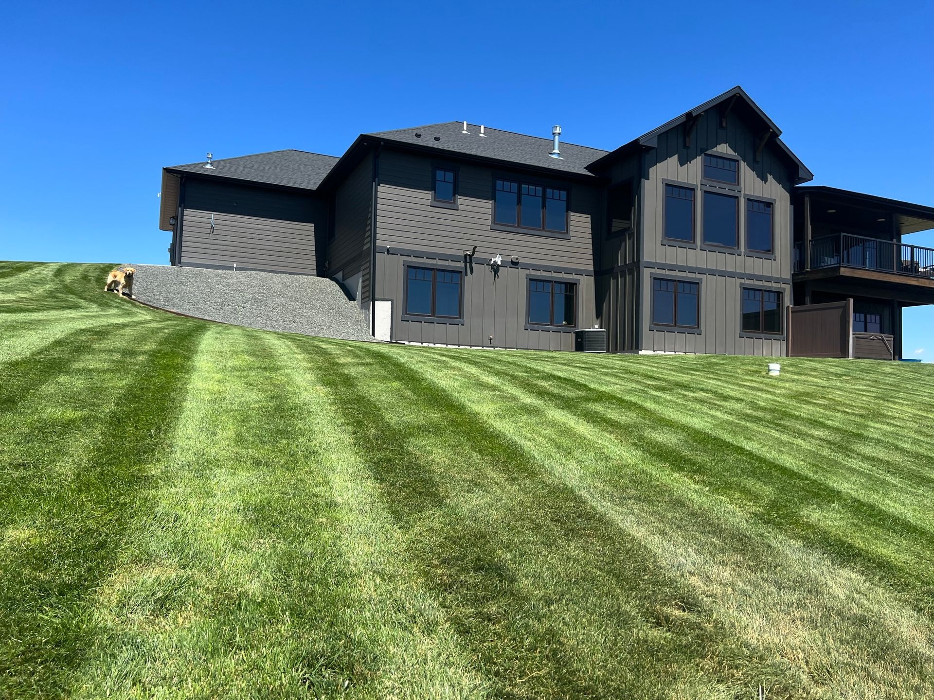 Dark gray house on a grassy hill with striped lawn under a bright blue sky.