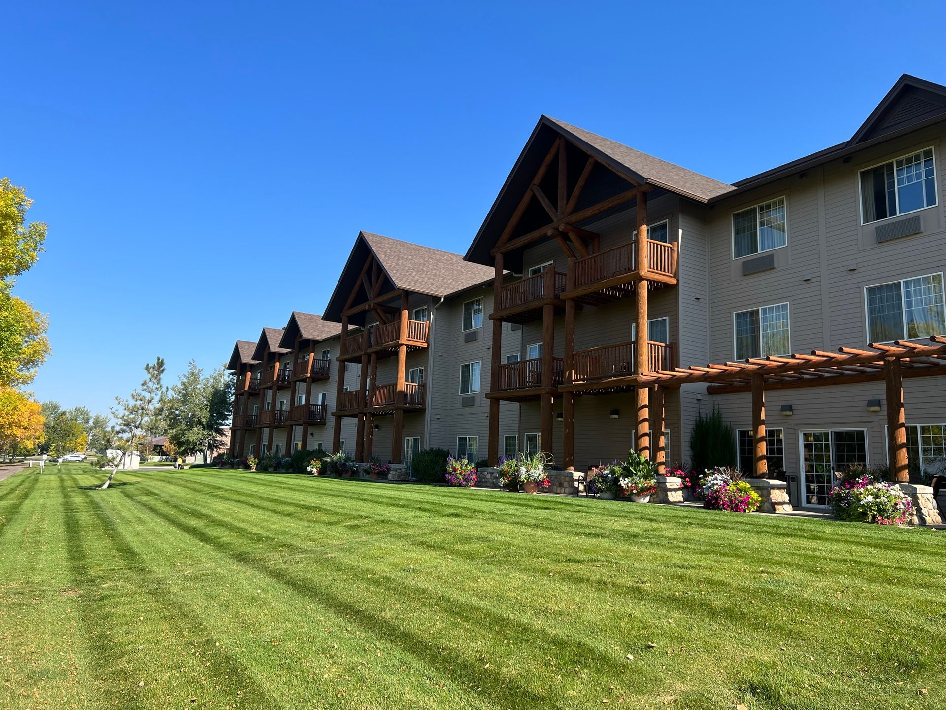 Apartment building with wooden balconies and brown roof against blue sky, green lawn.