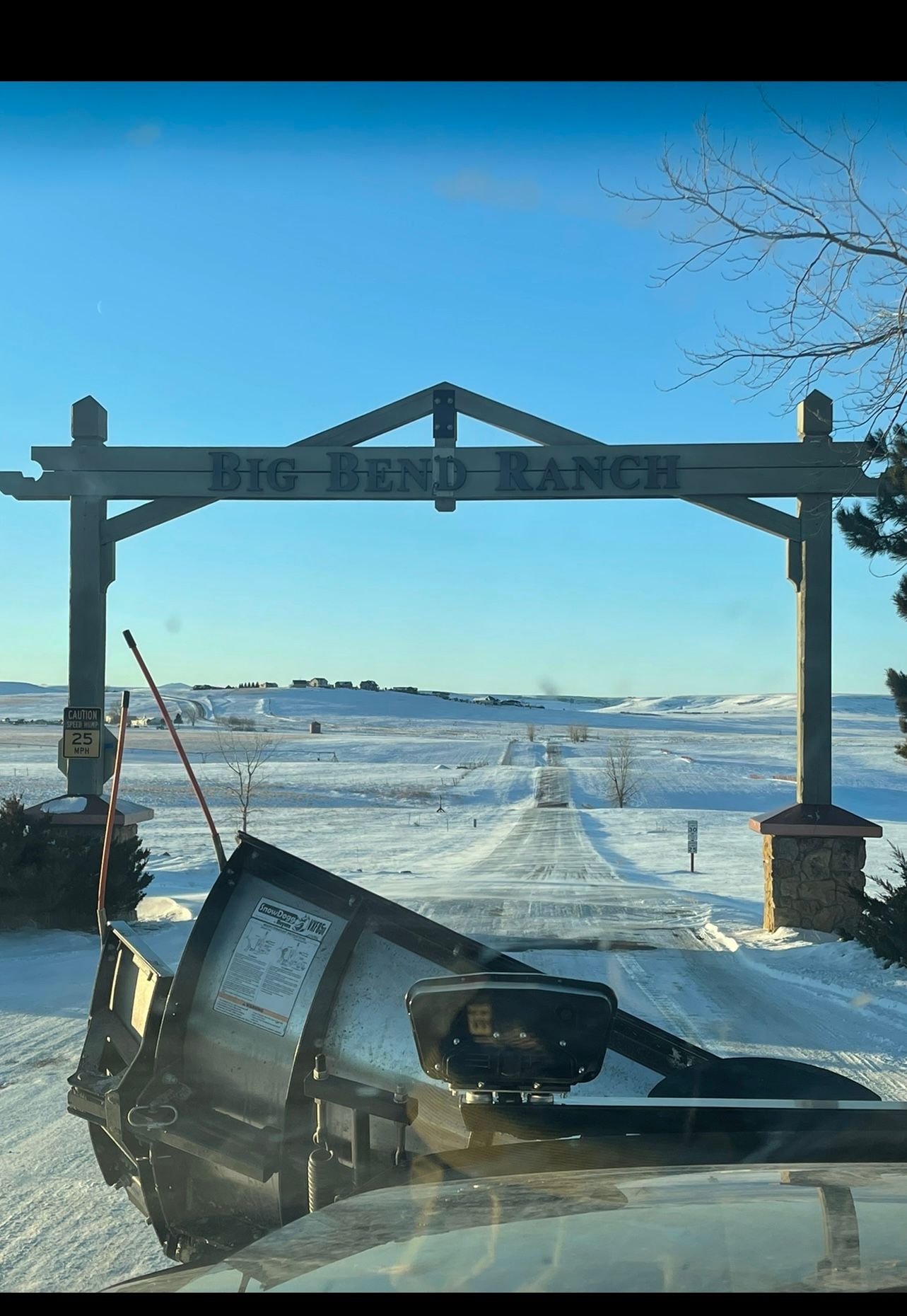 Big Bend Ranch entrance arch over snowy road. Clear blue sky. Snowplow in foreground.