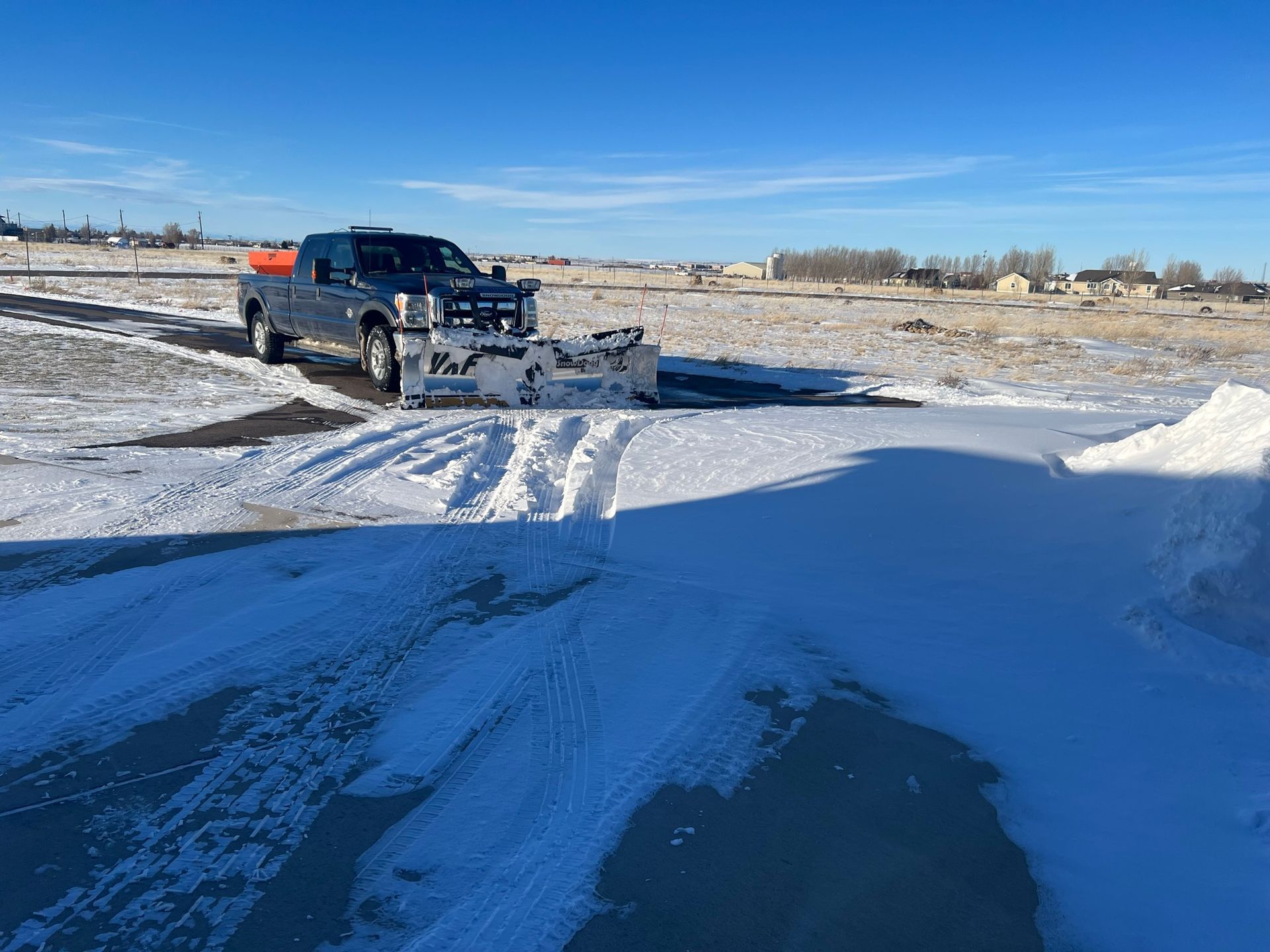 Snowplow truck clearing a snowy driveway on a sunny day.