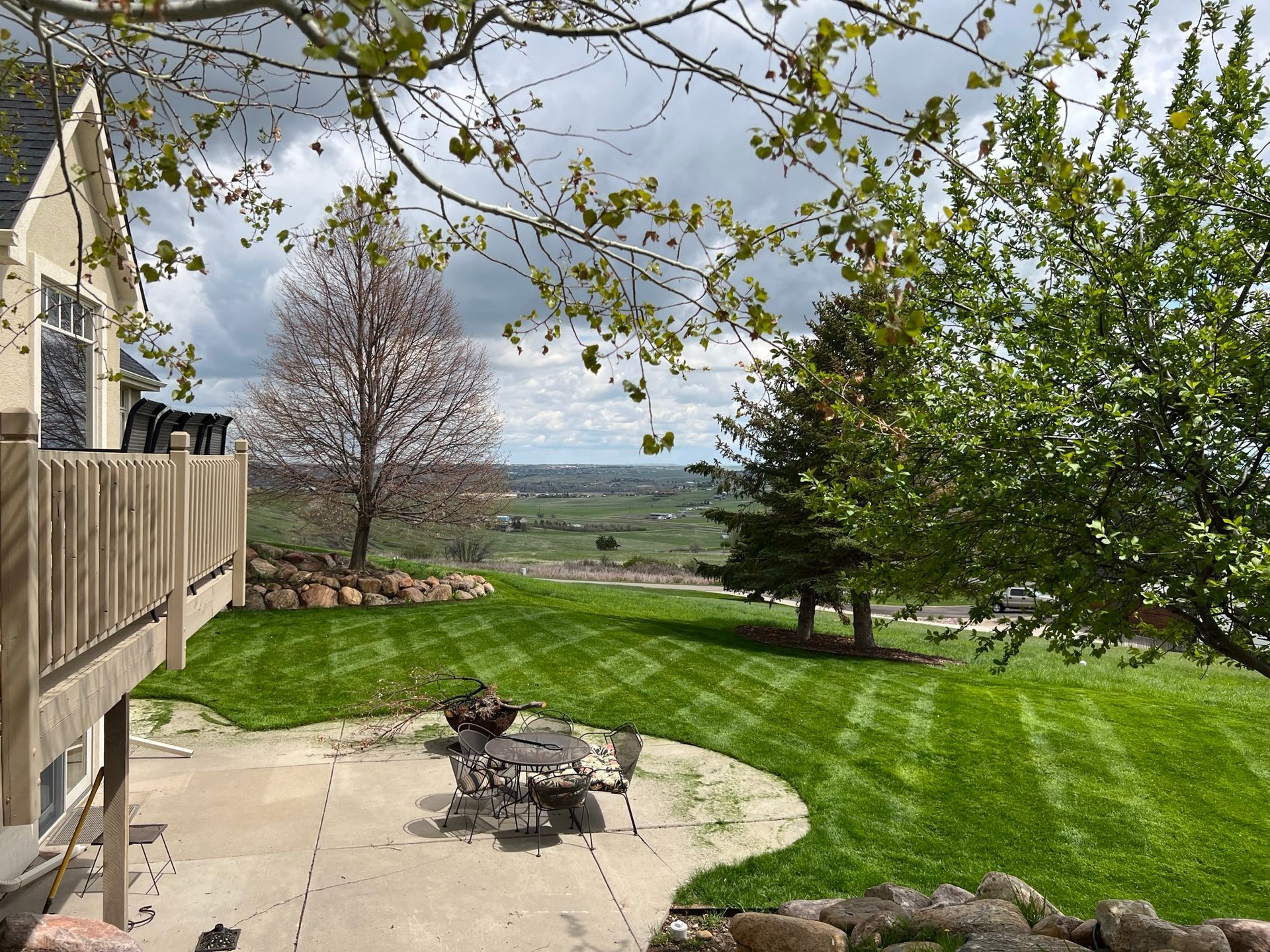 Backyard with green grass, trees, and a deck overlooking a scenic vista.