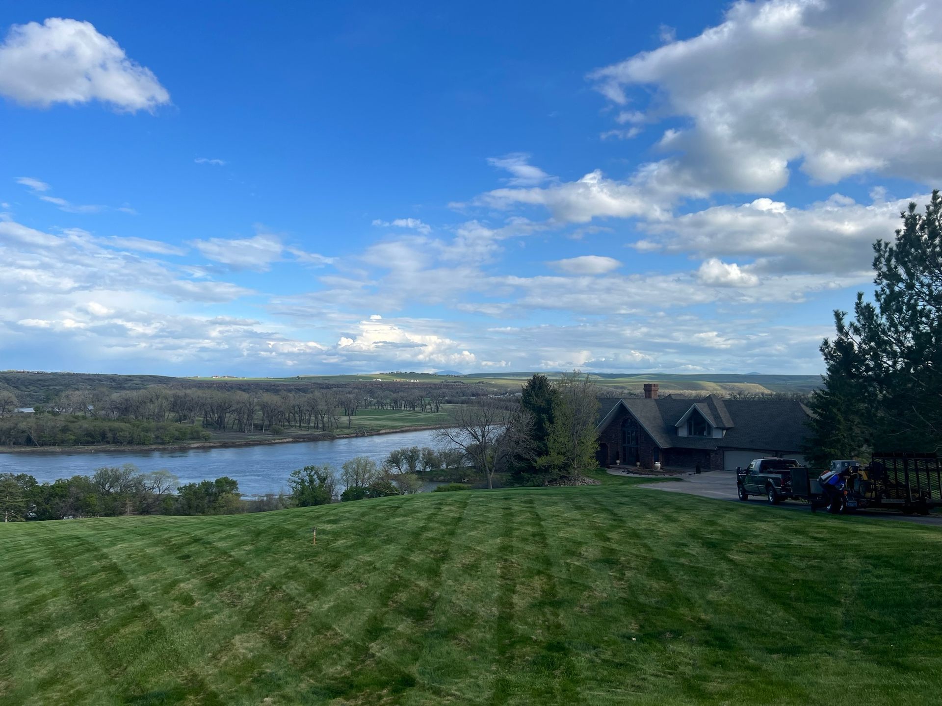 Green lawn overlooking a river and house under a cloudy blue sky.