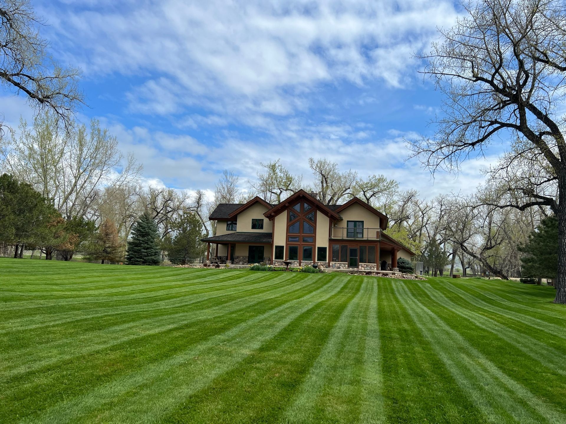 A large two-story house with a striped green lawn under a cloudy blue sky.