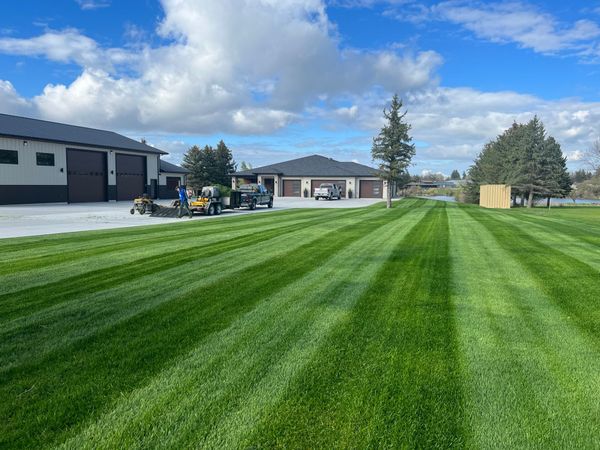 A lawn mower is cutting a lush green lawn in front of a house.