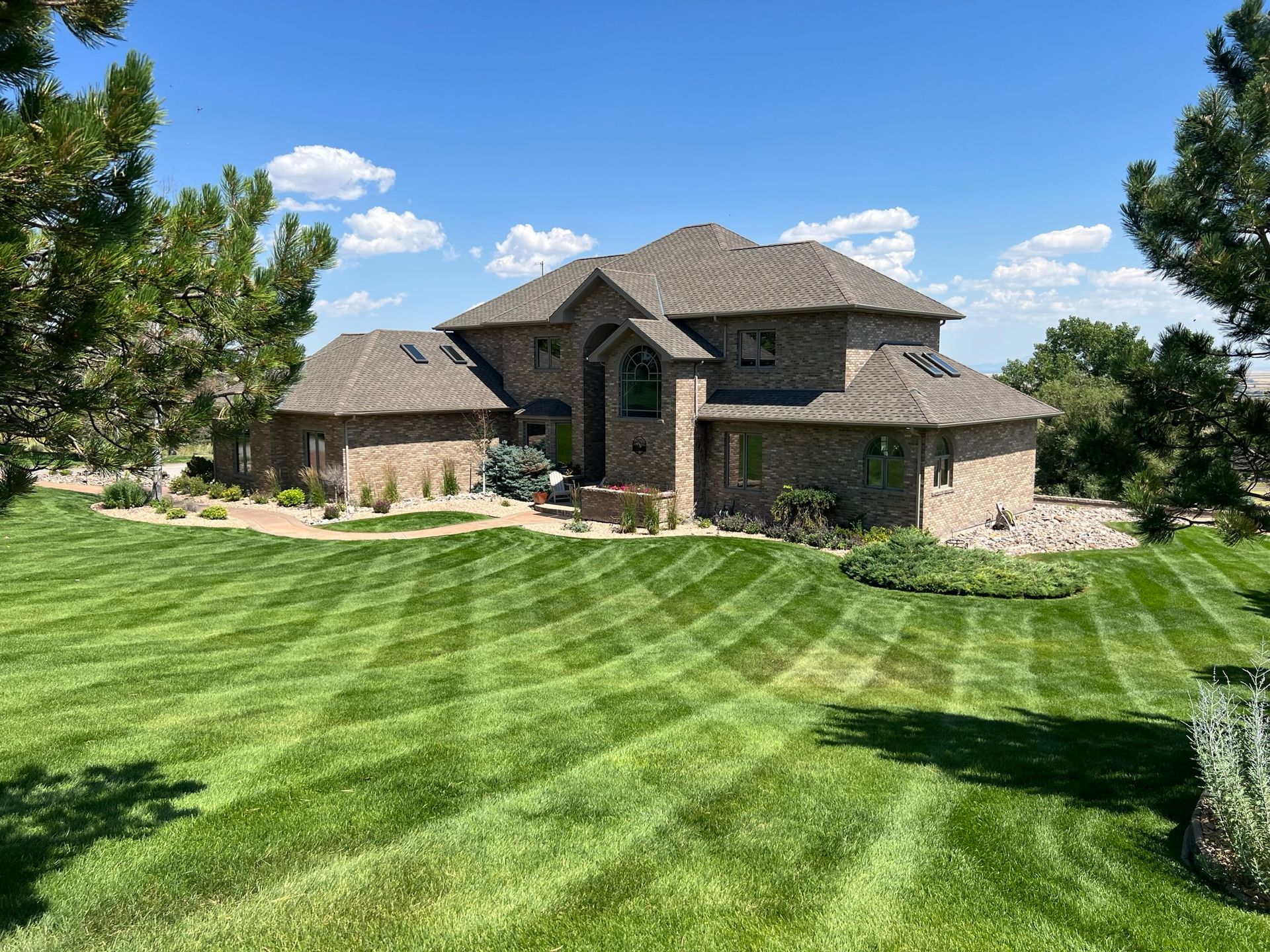 Large brick house with manicured lawn, green and blue sky.
