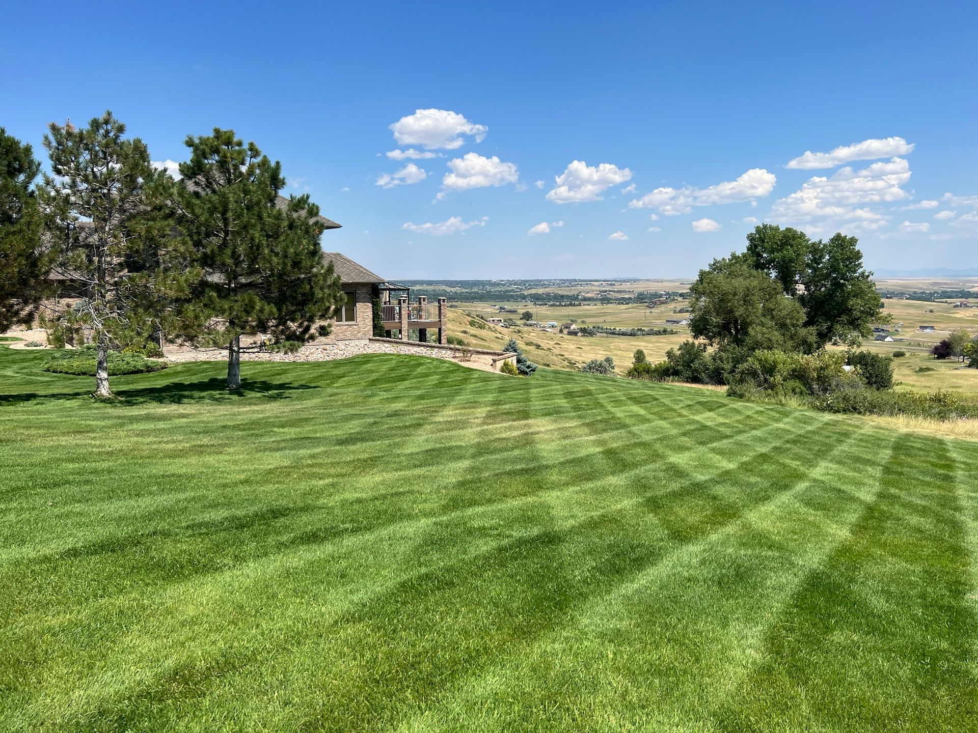 Green lawn with striped mowing pattern, overlooking a valley and distant city on a sunny day.