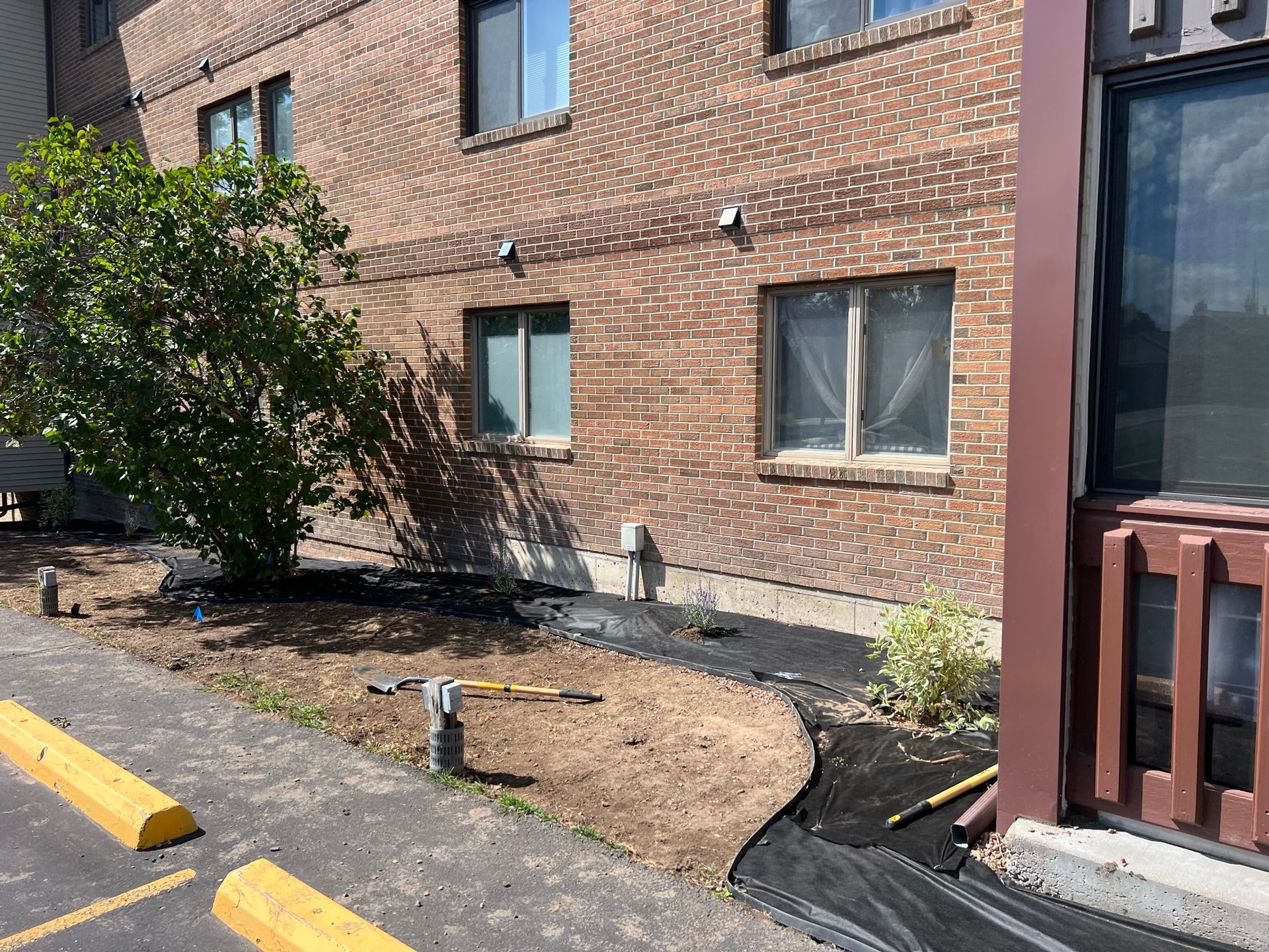 Brick building with newly planted garden bed along the foundation, parking lot to the left.