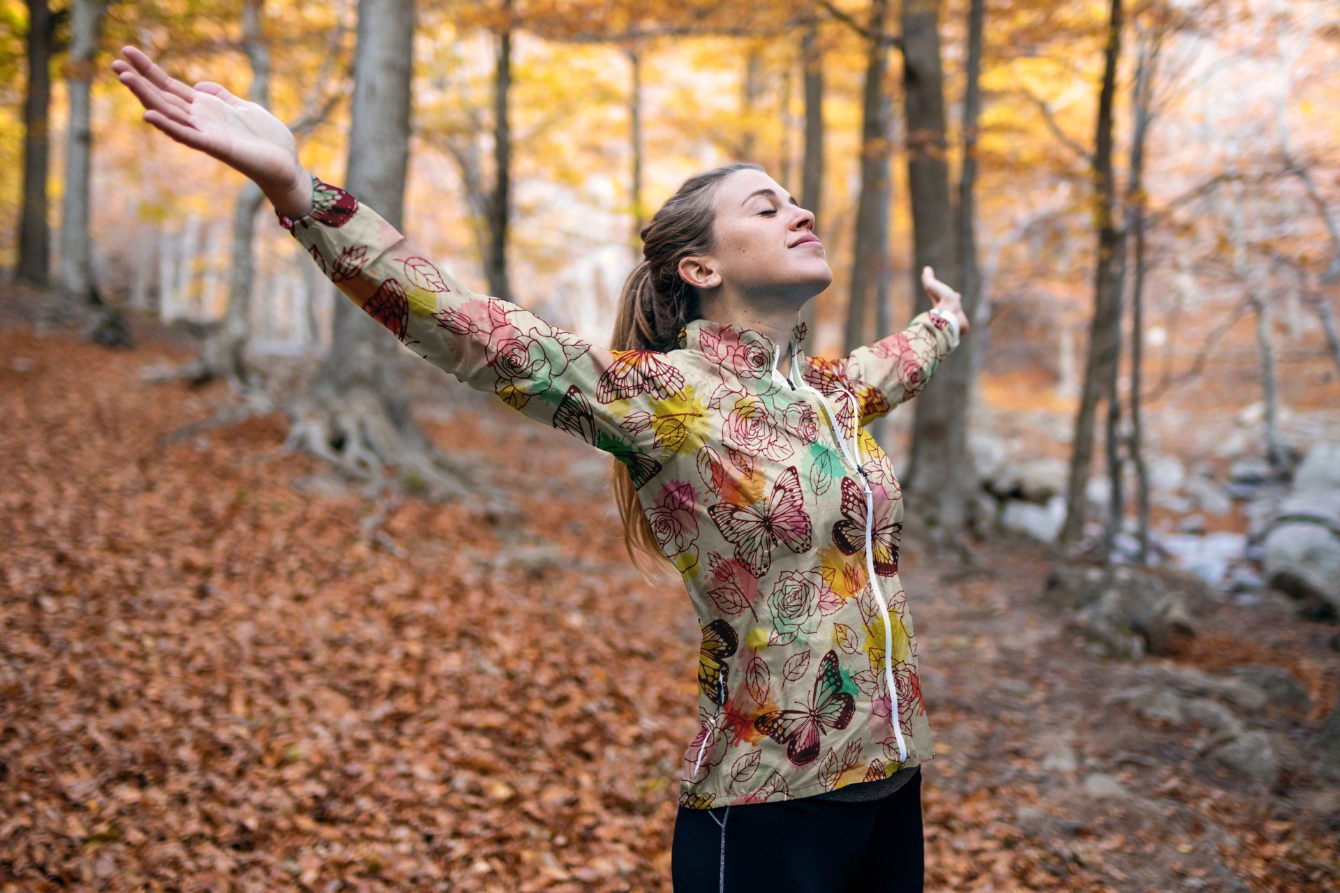 Woman standing in the autumnal woods wearing a long sleeve colourful printed top