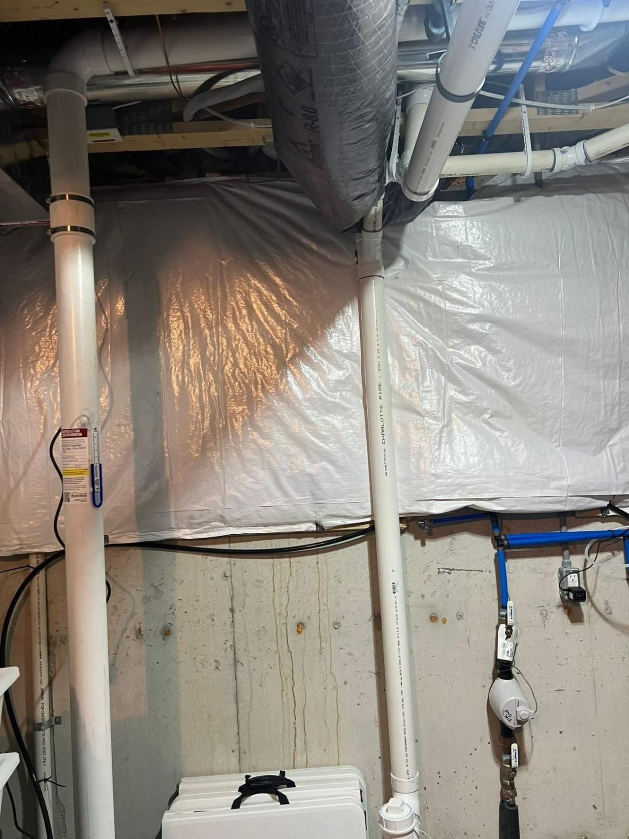 Pipes against a concrete wall with plastic sheeting and insulation. A blue water pipe is visible.