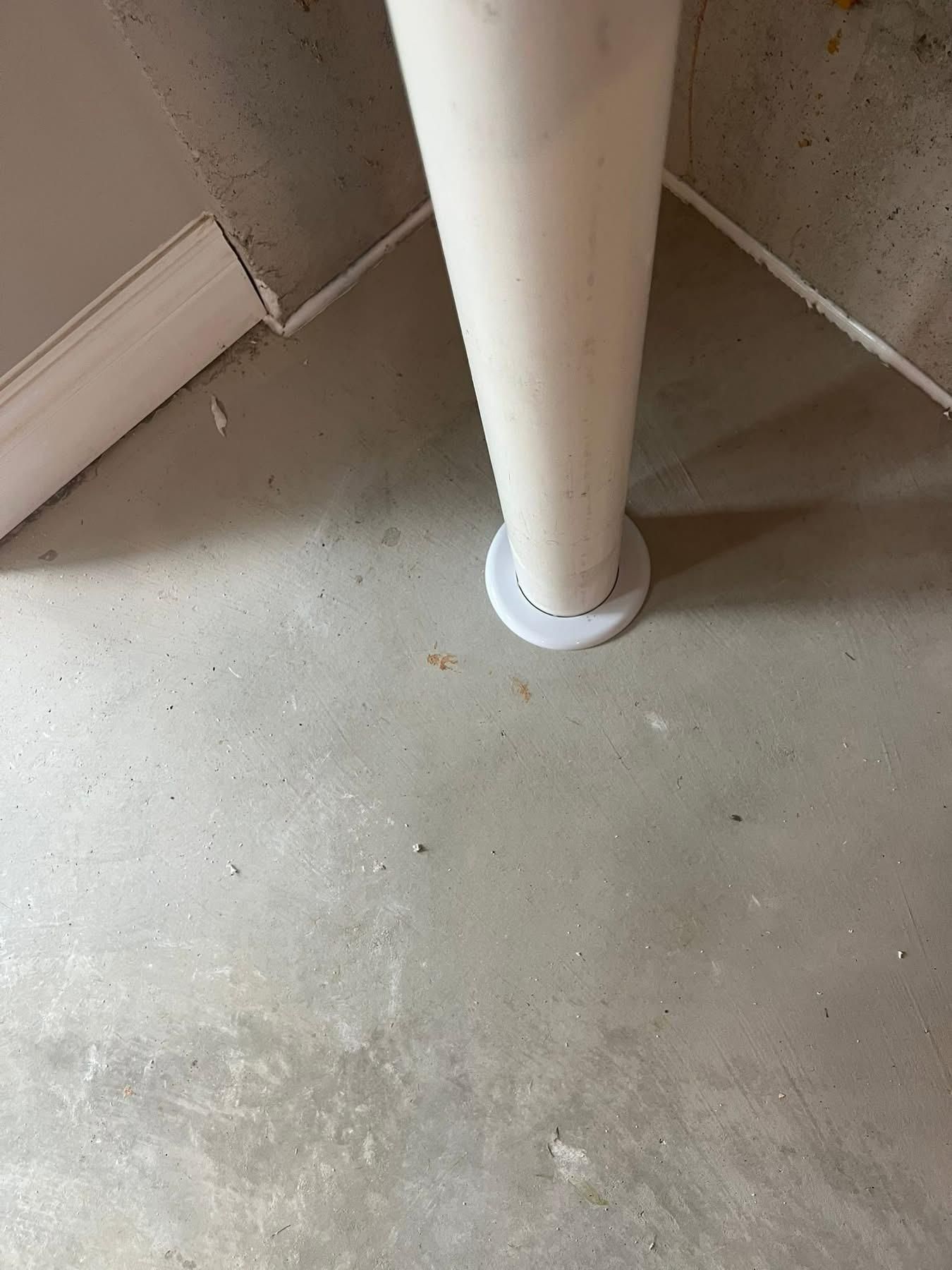 White pipe resting on a round, light-colored base on a concrete floor in a corner.