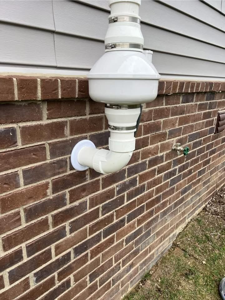White and beige pipe system attached to a brick wall, likely for drainage.