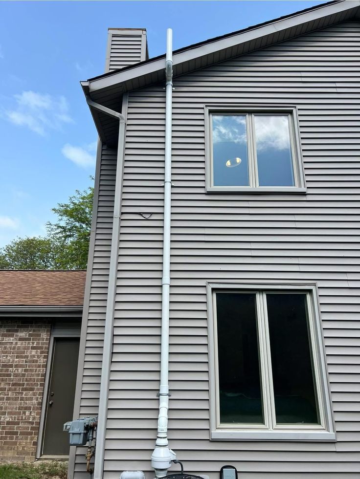 Tall white pipe attached to a gray house with windows, running from ground to roof.