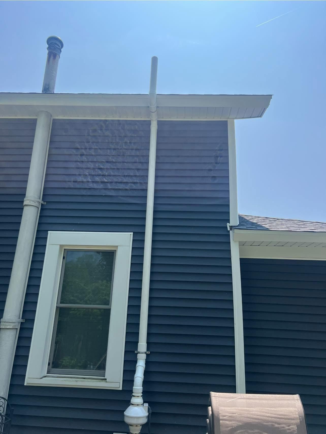 Dark blue house with a white window and a tall white pipe.