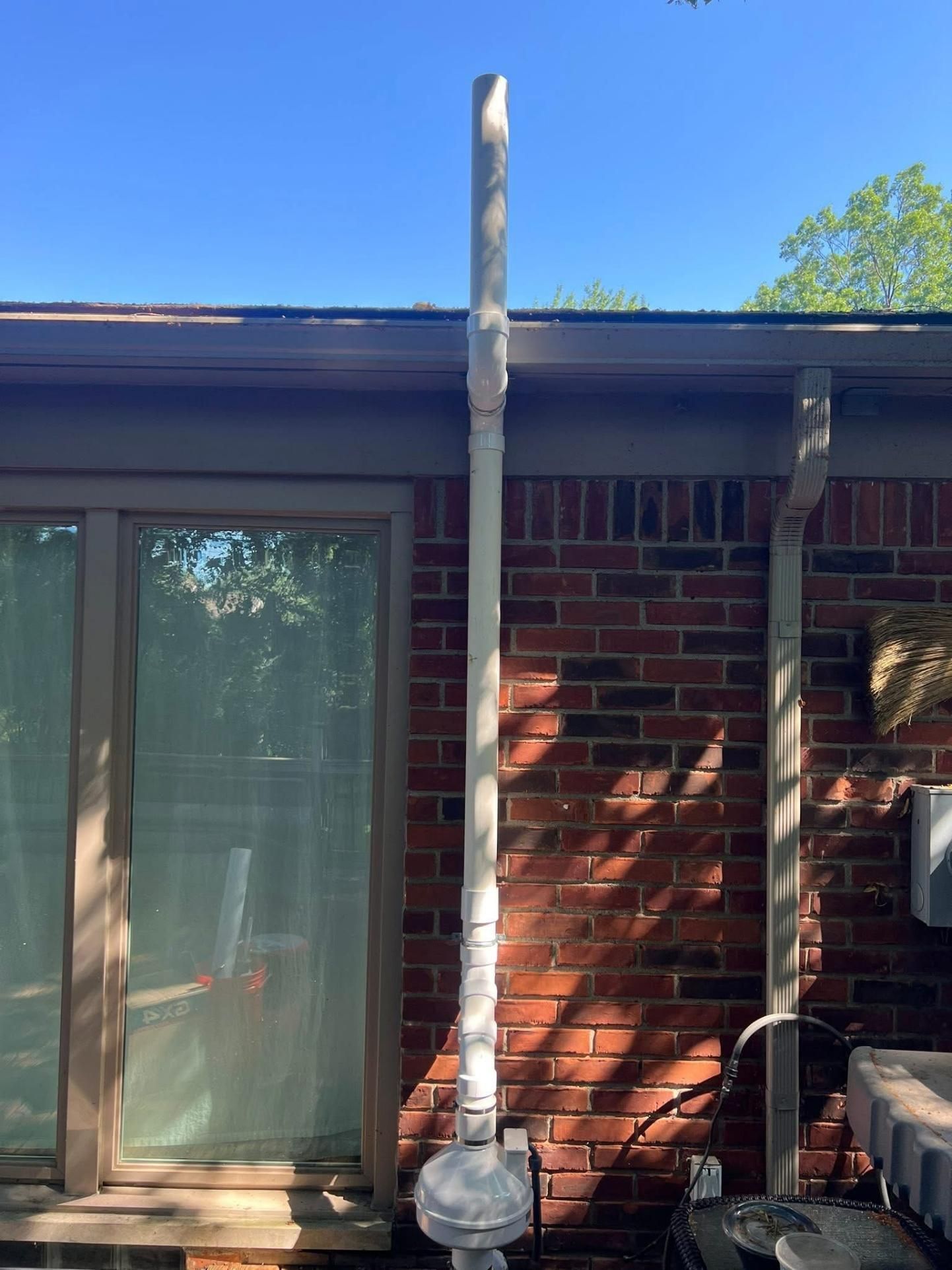 White vent pipe extends up the brick wall of a house, next to a sliding glass door.