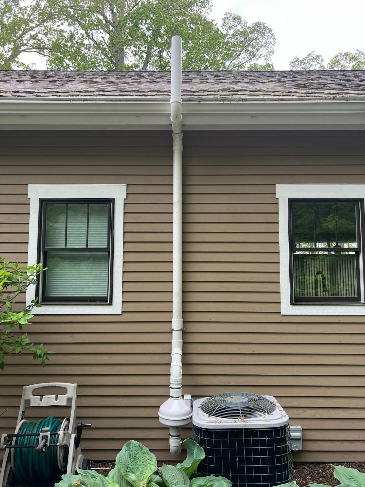 White pipe antenna attached to a brown house, next to windows and a/c unit.