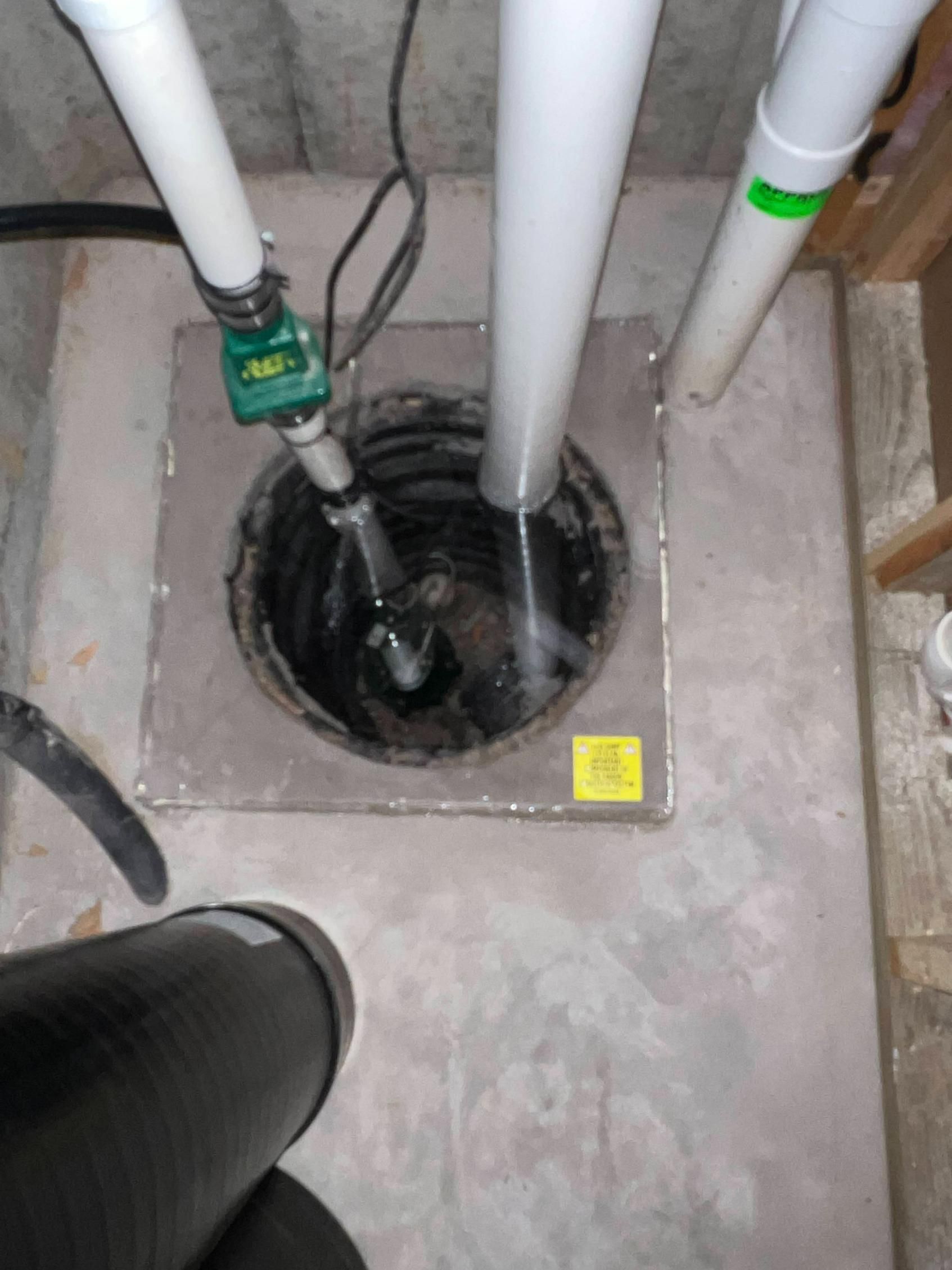 Basement sump pump with piping, electrical cord, and a square cover. Black, white, and gray.