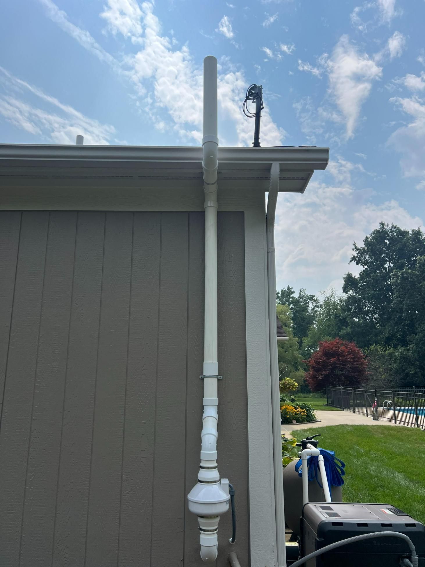 White pipe extending up a tan building. The pipe ends with a cap near the roof. Sunny outdoor setting.