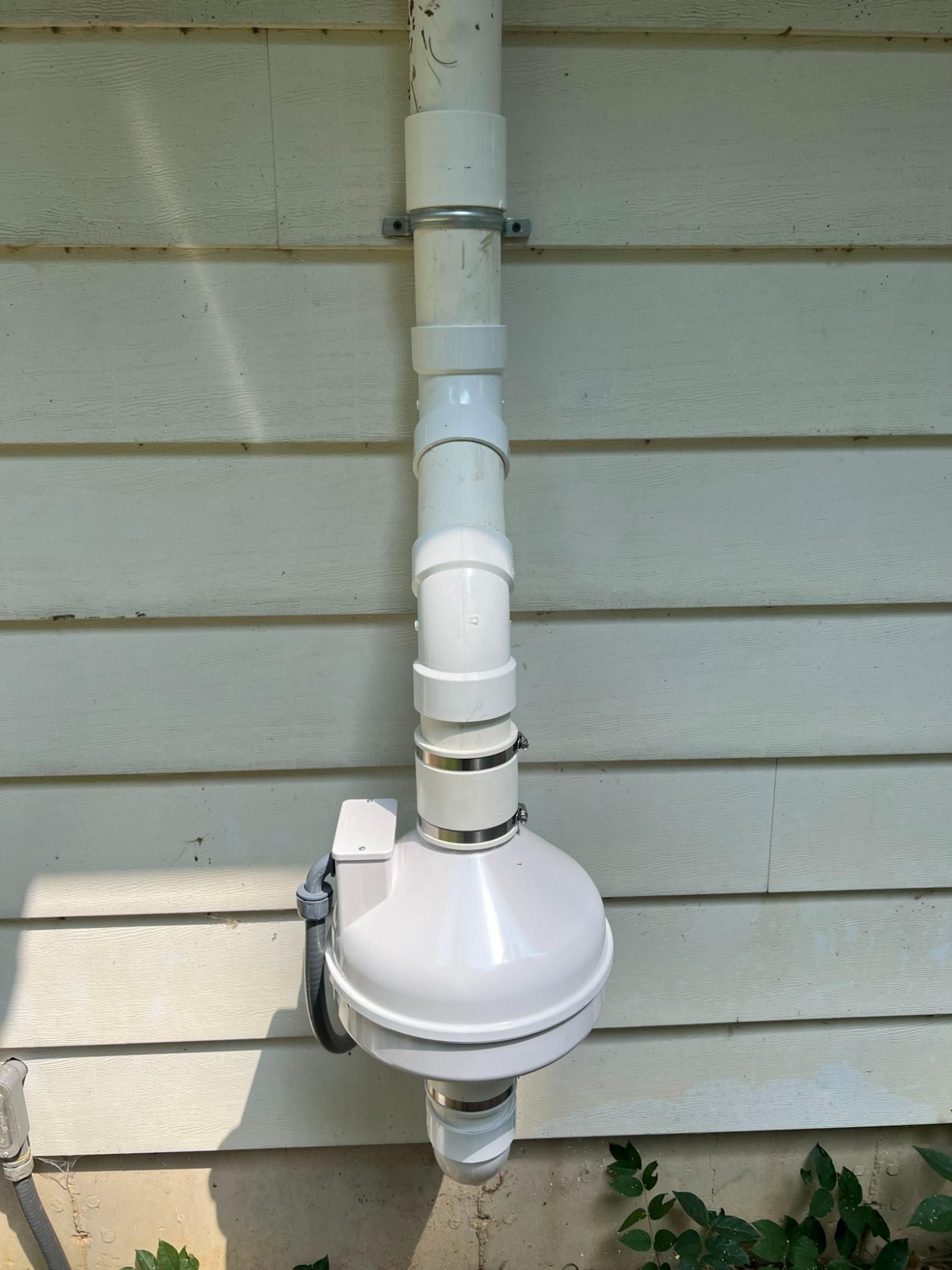 White plastic downspout with a rounded, box-like structure attached to a building.