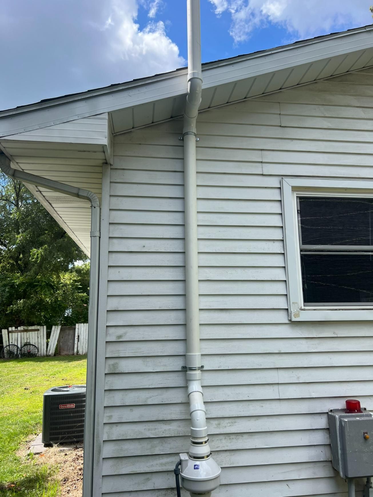 A white pipe runs along the side of a white building, reaching up to the sky.