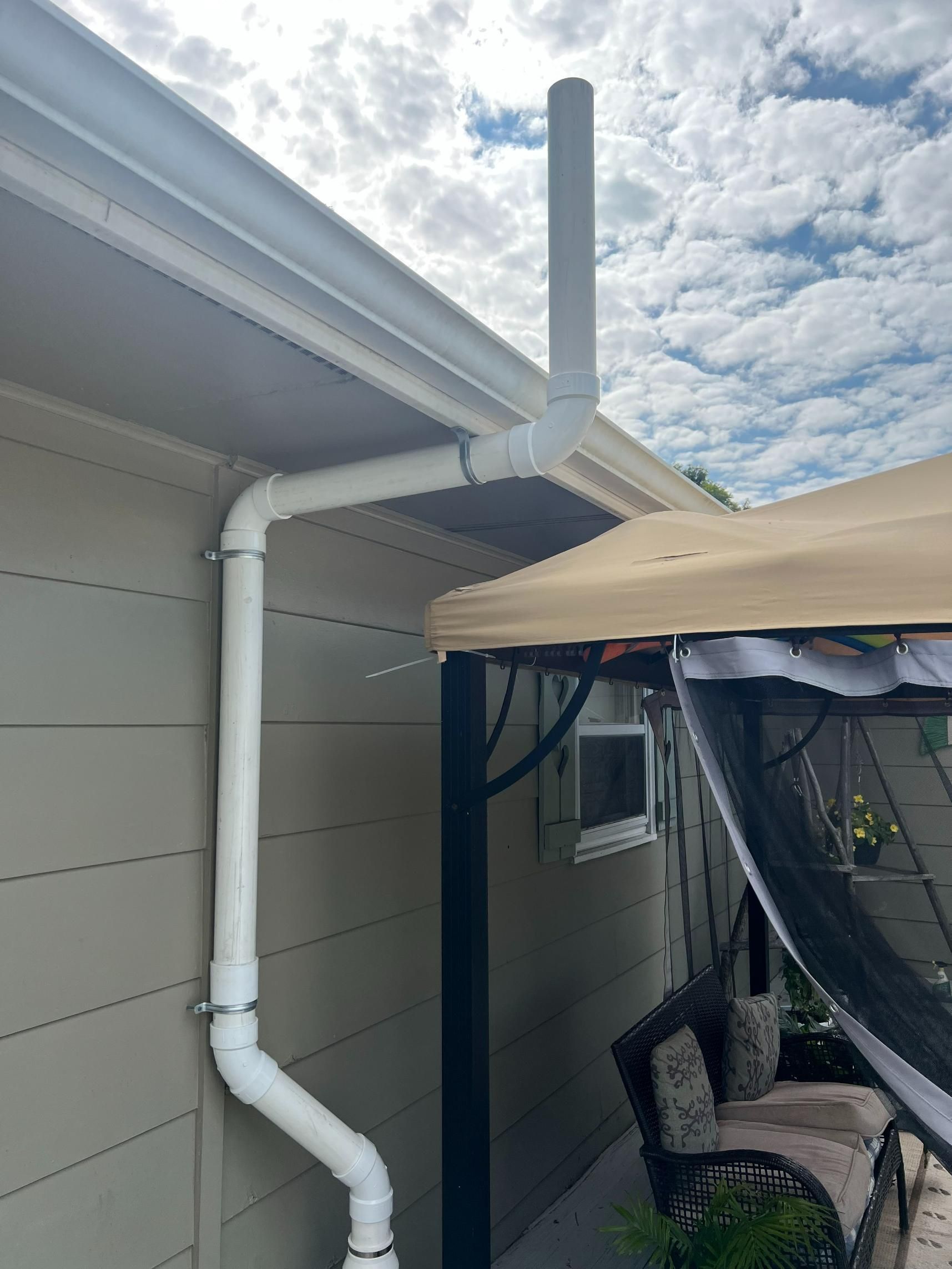 White rain gutter system on the side of a building with an extended vertical pipe. Cloudy sky.