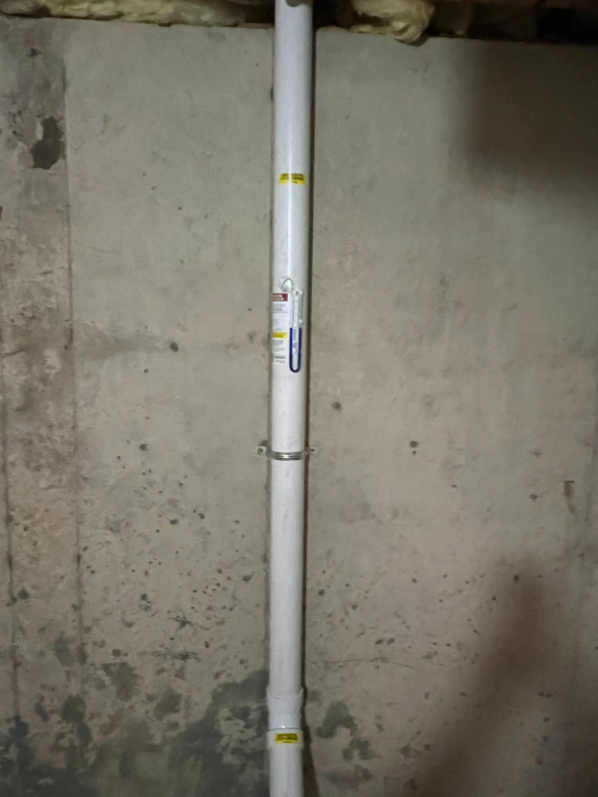 White PVC pipe secured against a gray concrete wall with metal clamps.