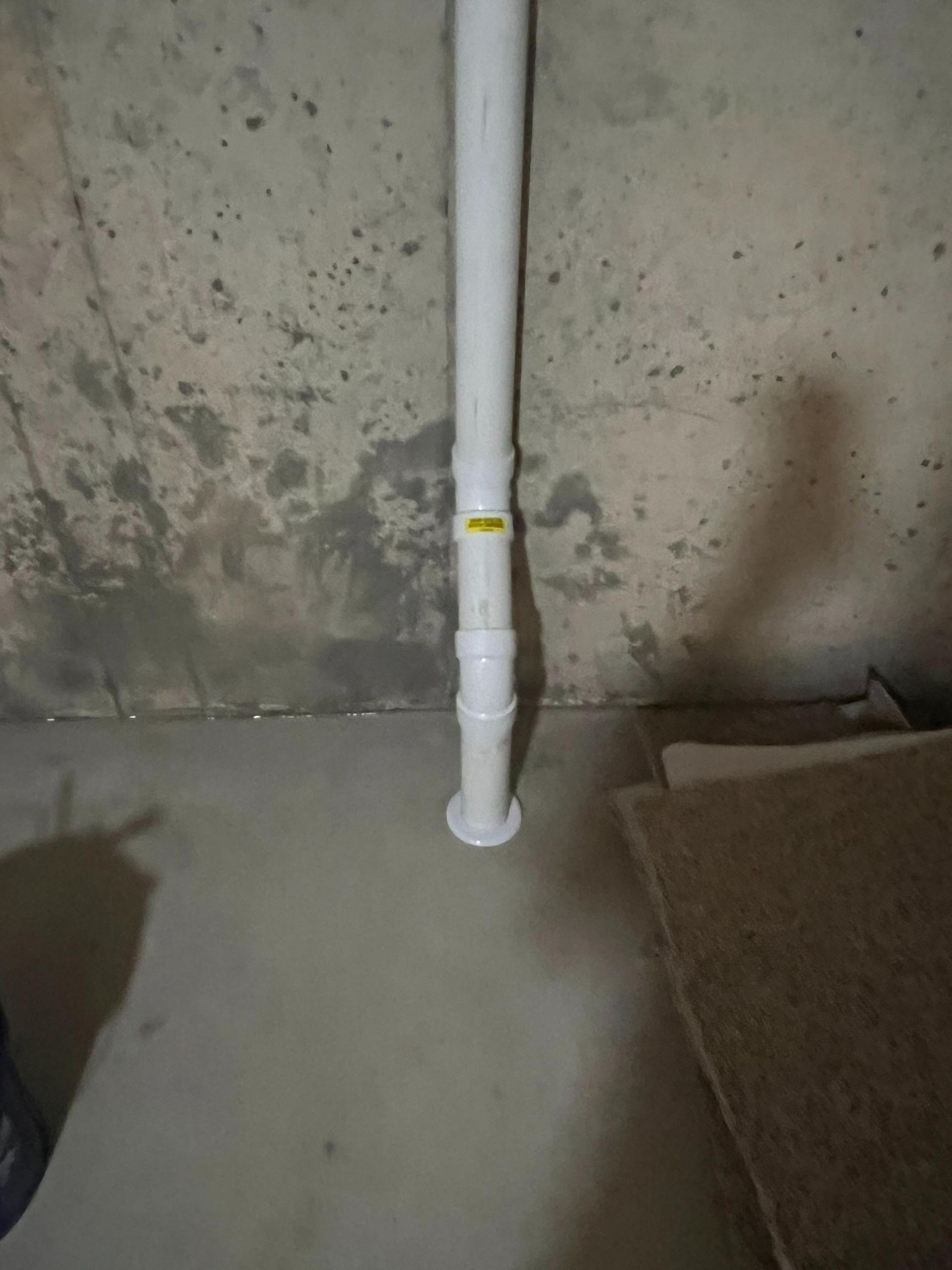 White drain pipe against a dirty, stained concrete basement wall.
