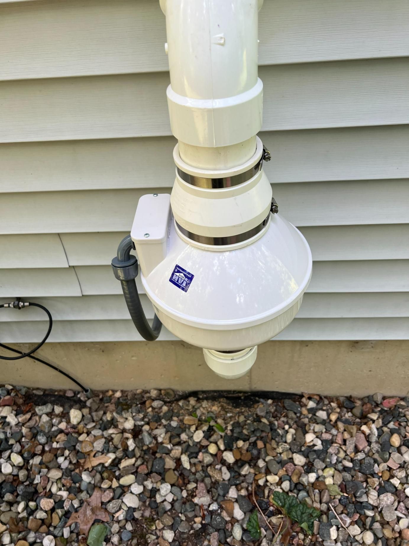 White radon mitigation system attached to a house's exterior wall.