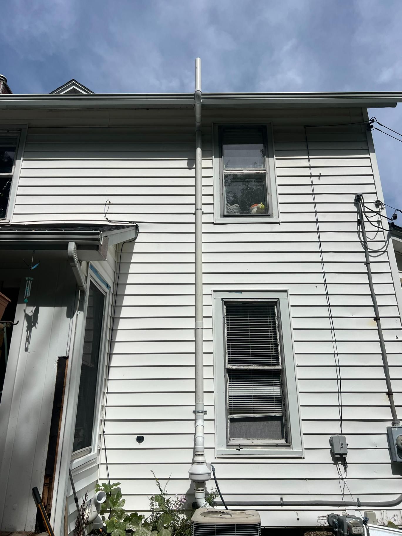 Side of a white house with two windows, a gutter, and a pipe.