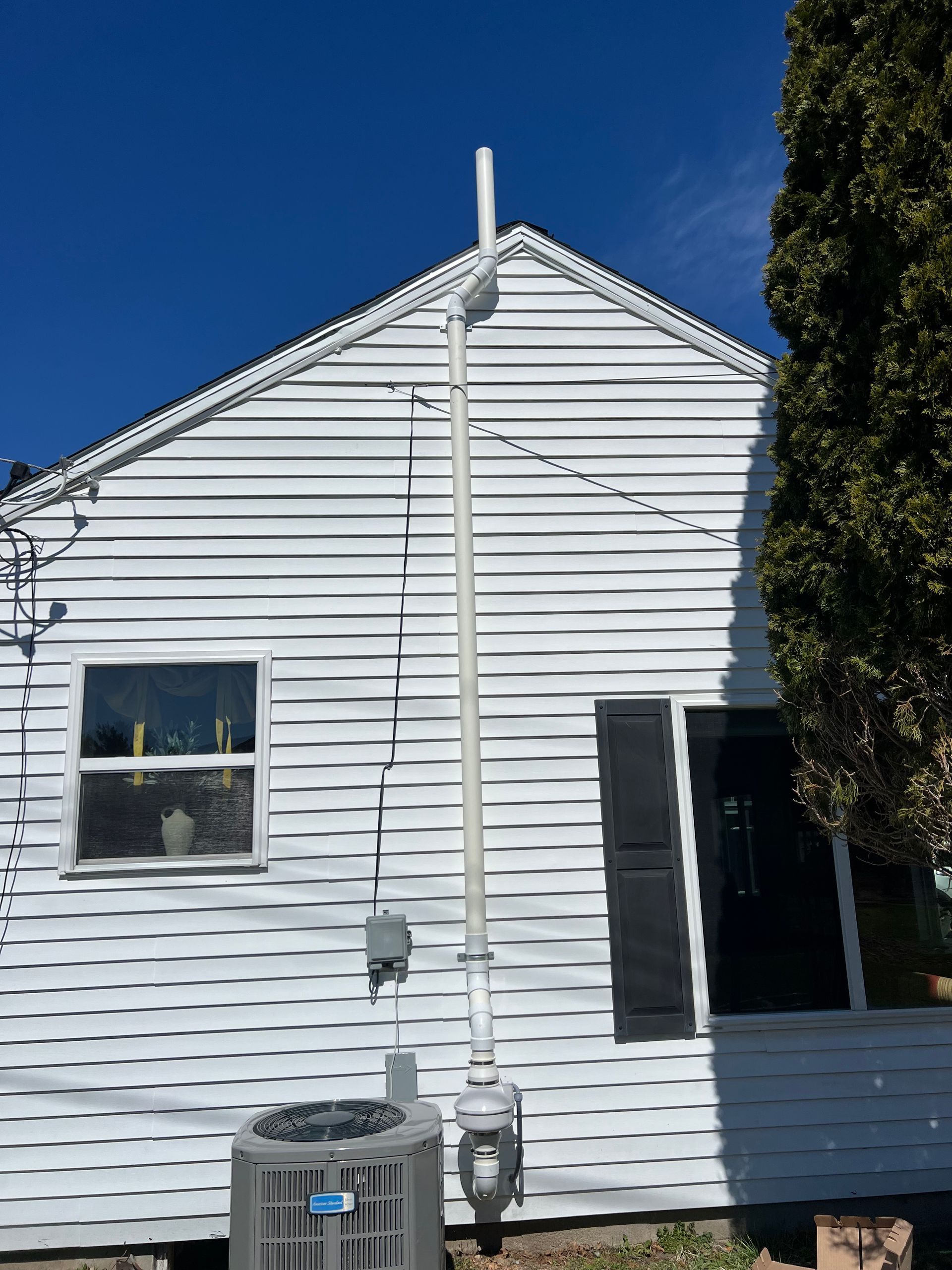 Tall white pipe attached to a gray house with windows, running from ground to roof.