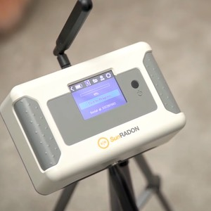 A white SunRADON device on a tripod, displaying a menu on its screen, with an antenna.