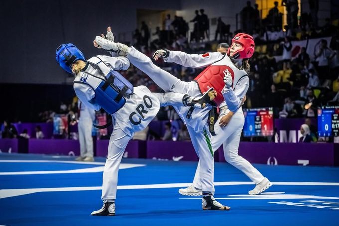 Bambini in uniforme bianca da arti marziali posano in un dojo con medaglie e un trofeo su tappetini blu.