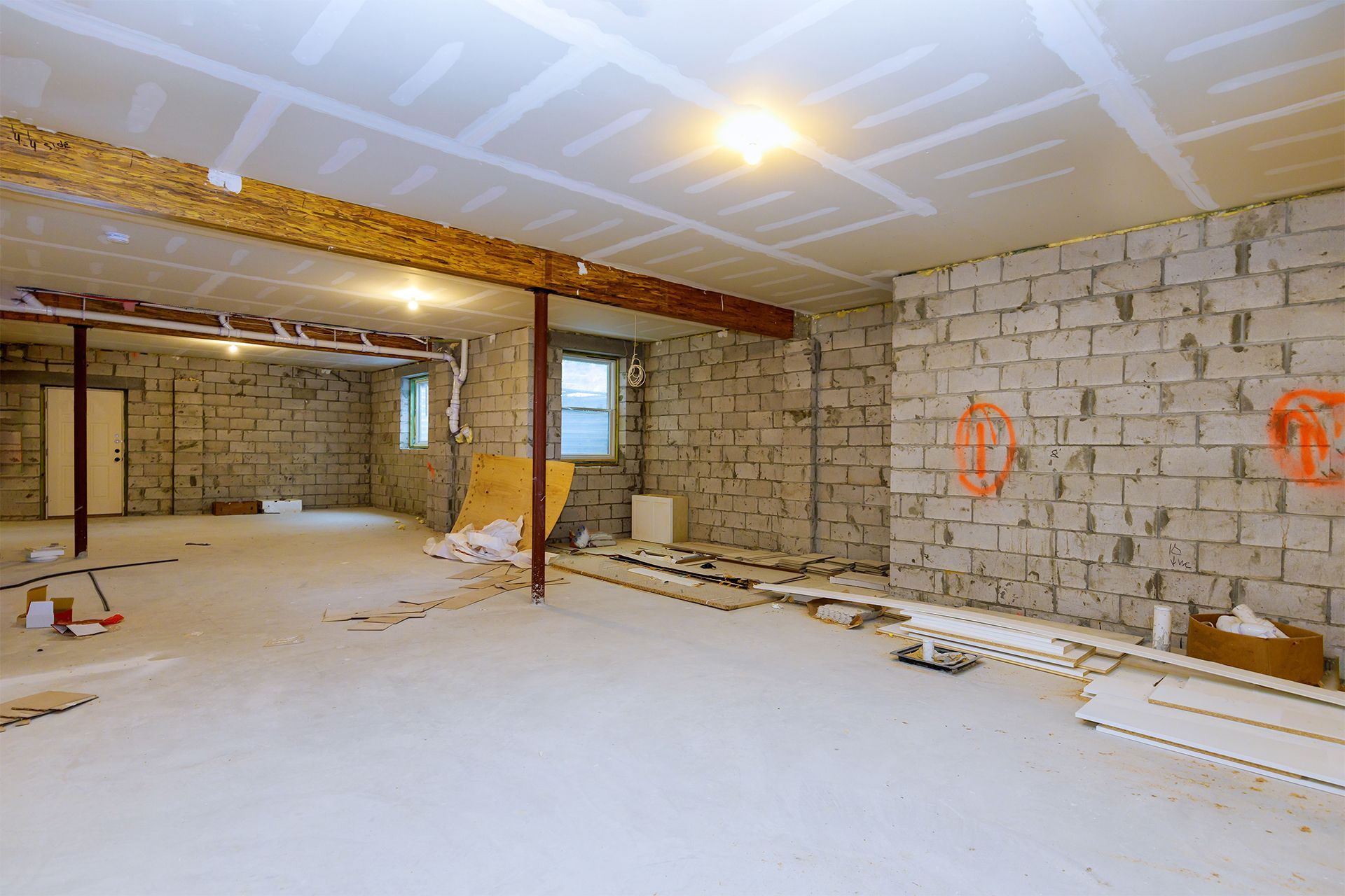 A large unfinished basement with exposed concrete block walls, a drywall ceiling, and support beams.