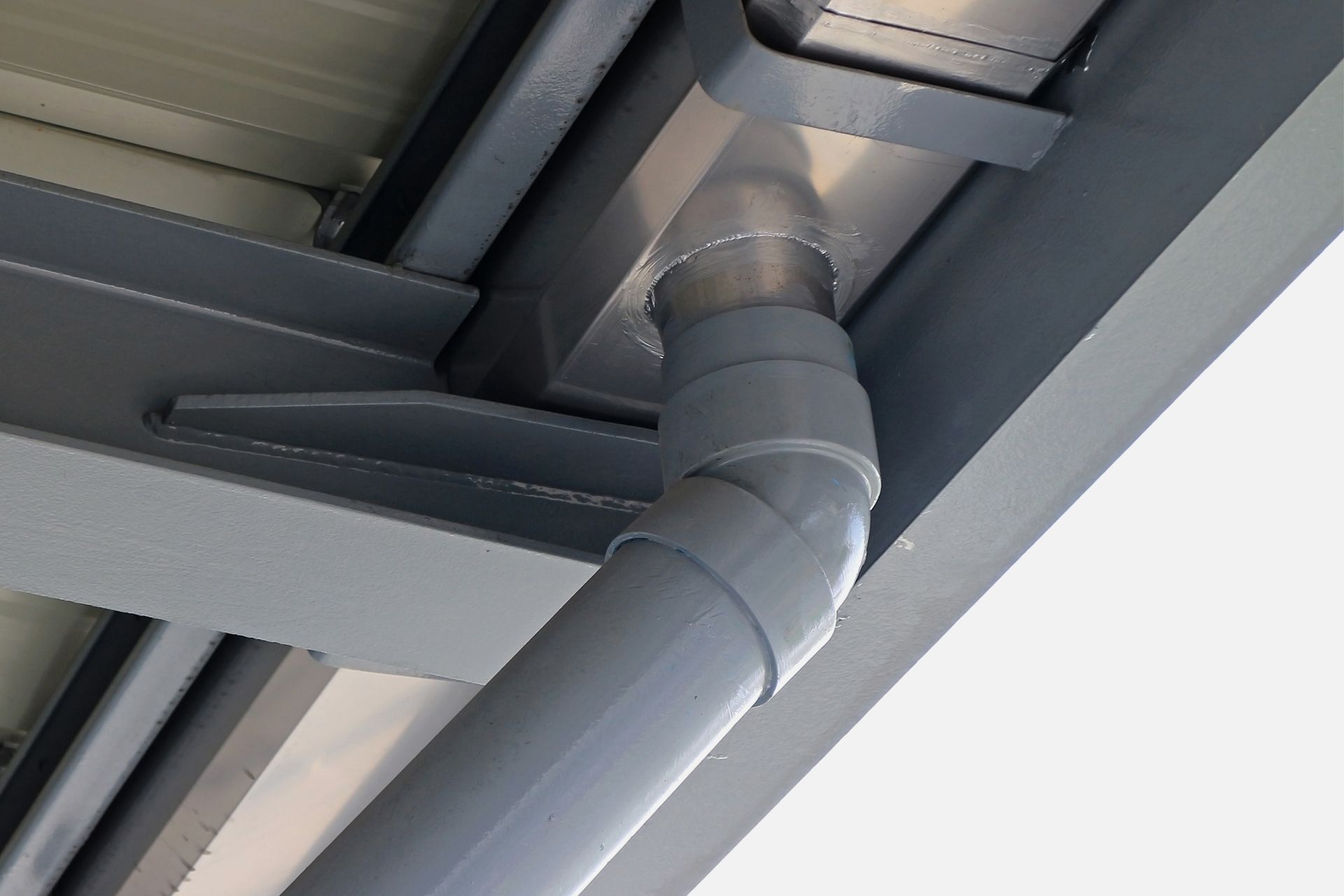 A gray downspout attached to a metal gutter system on the underside of a roof structure.