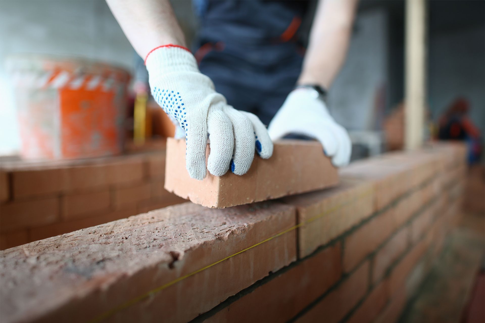 A construction worker wearing gloves places a brick onto a wall under construction.