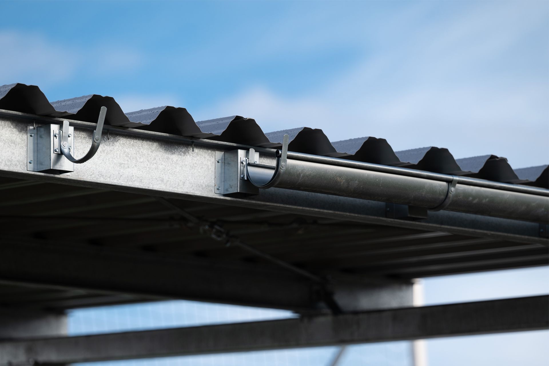 A close-up view of a metal roof edge with a gutter system installed against a blue, cloudy sky.